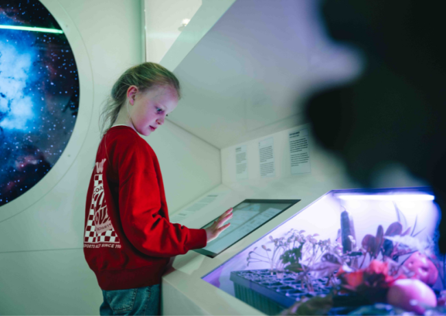 Meisje in rode trui die een touchscreen bediend in de zone De Planeer